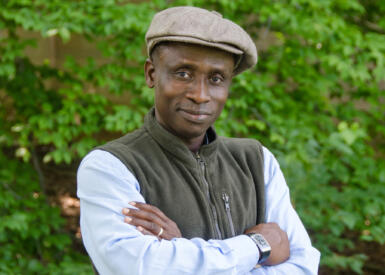 Akin Adesokan stands for a headshot with his arms crossed in front of greenery.