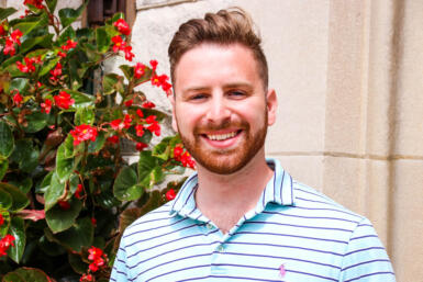 A headshot of Johnathan Anderson in front of greenery and a stone wall.