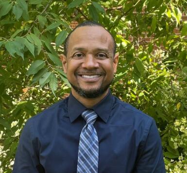 Headshot of Novotny Lawrence in front of greenery.