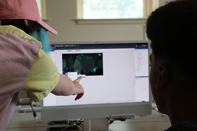 A Game Development Camp counselor points at a computer screen while helping a student.