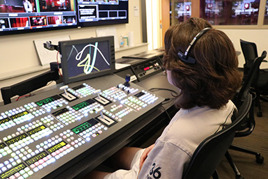 A student wearing headphones sits in front of a switcher in the Ed Spray Control Room.