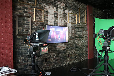 A film camera is recording while projecting the contents onto a screen mounted on a brick wall.