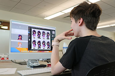 Student stares at computer screen, which has character models up for a game.