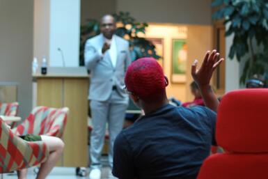 Person sits in a chair with their hand raised while Ron Nixon stands in the background pointing at the person.