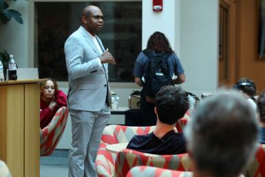 Ron Nixon stands in the middle of the Franklin Hall commons talking to students who are seated surrounding him.