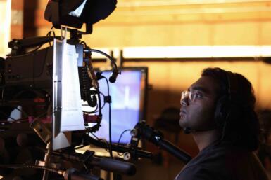 Person operates a large TV camera with a clipboard hanging to the side.