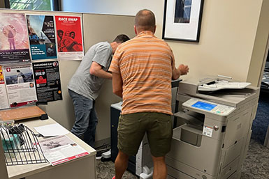 Two men lean over a printer in the BFCA office. 