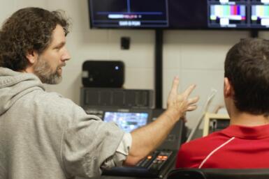 Two people sit in front of computers and TVs orchestrating a live broadcast.