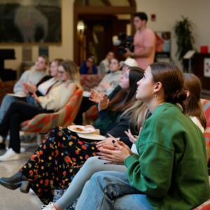 Several people are seated and are clapping in Franklin Hall commons. 