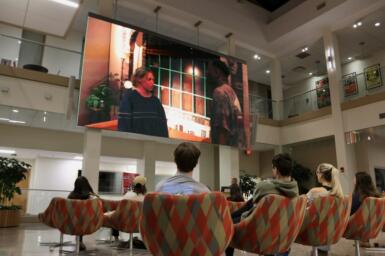 Crowd sits in the Franklin Hall commons watching a movie displayed on the large screen.