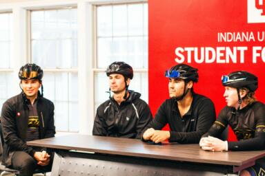 Four people wearing bike helmets sit at a table
