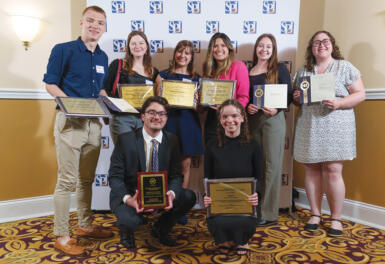 Eight students hold awards in front of am SPJ backdrop.