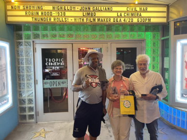 Three people stand in front of doors to a movie theater.