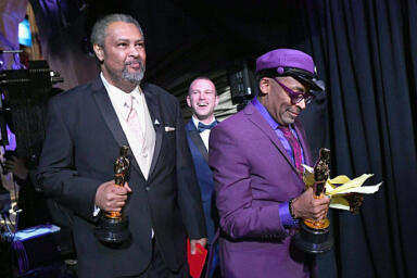 Two people stand in backstage holding awards.