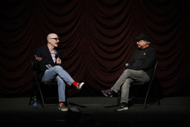 Two men, David Tolchinsky and Michael Uslan, sit opposite to each other on a stage.