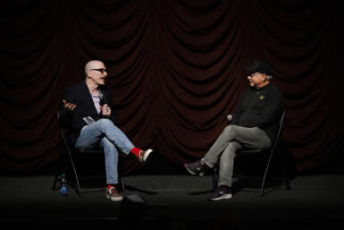 Two men, David Tolchinsky and Michael Uslan, sit opposite to each other on a stage.