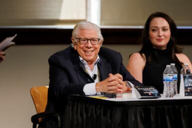 Carl Bernstein is seated at a table on a stage and smiles out to an audience.