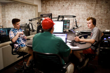 Three students recording in a radio booth.