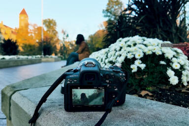 A camera sits on a stone edge of a flowerbed and captures Ahmed Tahsin Shams sitting.