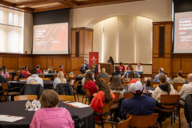 People sit at tables and look toward the front of the room.