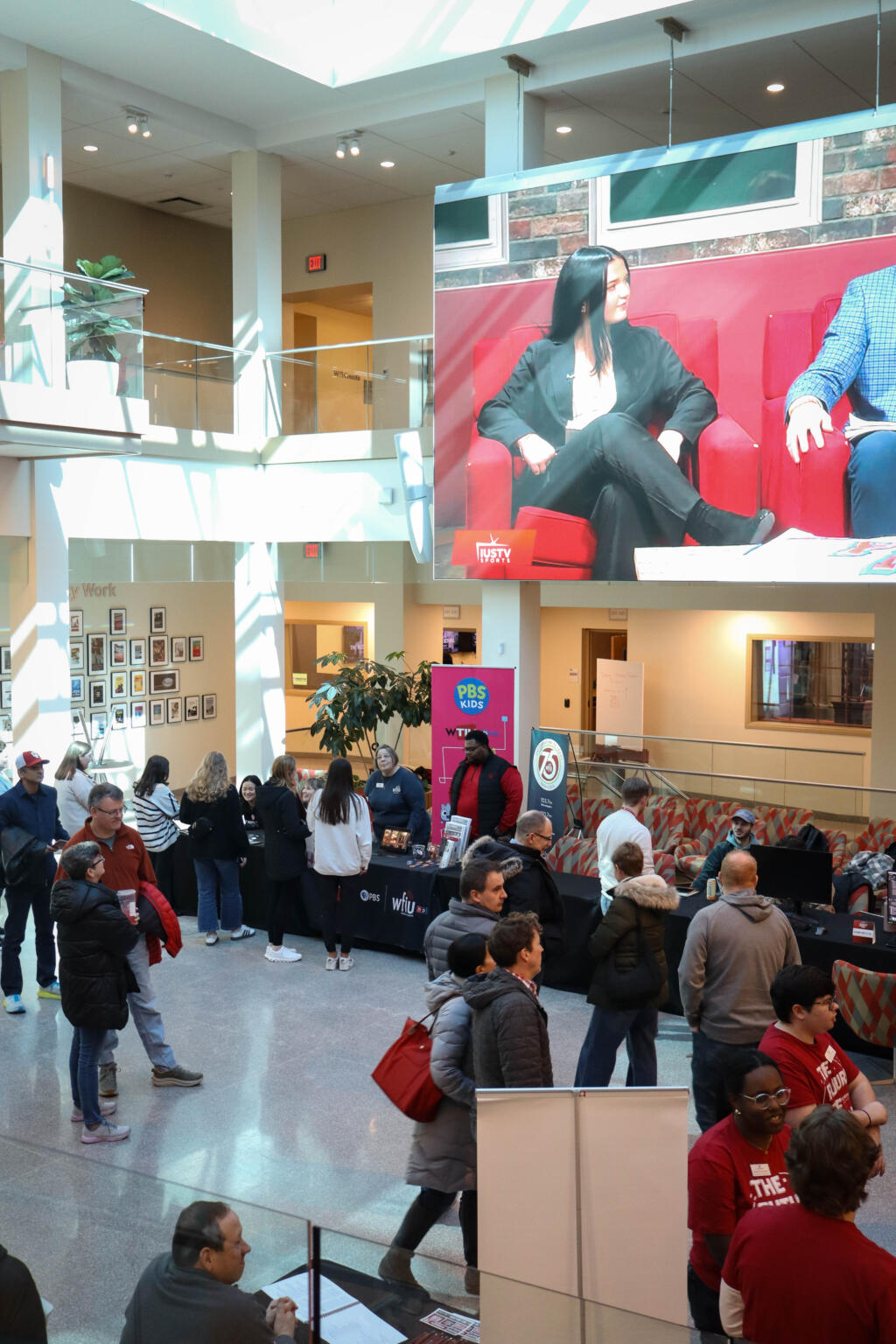 People stand and sit at tables in Franklin Hall commons beneath a large screen.