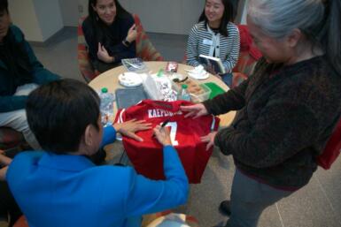 Maria Ressa signs the back of a jersey while seated at a table with several people standing and sitting around it.