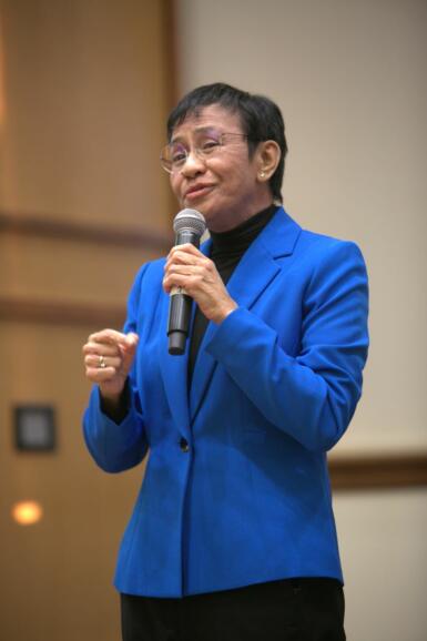 Maria Ressa stands on stage with a microphone in her hand.