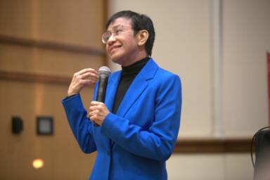 Maria Ressa stands on stage holding a microphone.