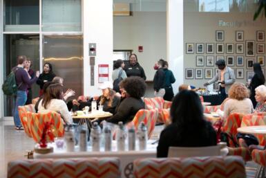 Wide shot of several people either standing in Franklin Hall commons or seated around several tables. The wall to the far right has several pictures displayed.