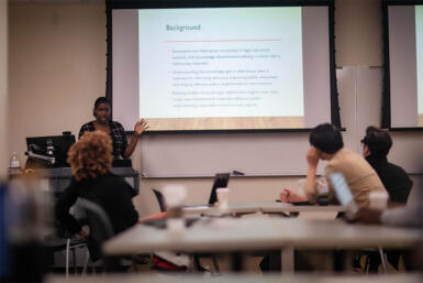 Trizah Ombewa presenting her research at the front of the classroom.