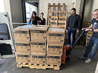 People stand around moving boxes stacked ontop of each other.