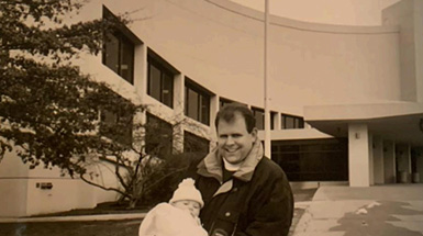 Person holds a baby while standing outside Assembly Hall.