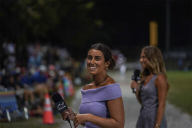 Picture of Kara Adams holding a mic and reporting with another reporter in the background.