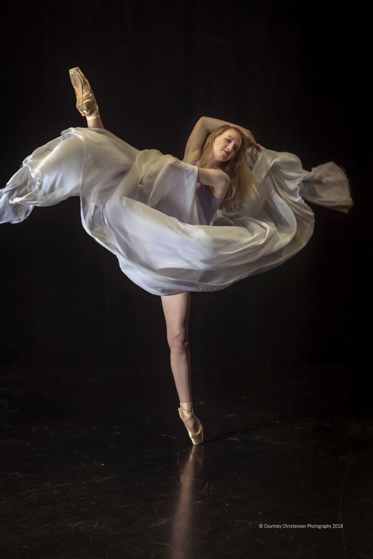 Ballerina wearing a flowing outfit stands on their toe with the skirt billowing around them.