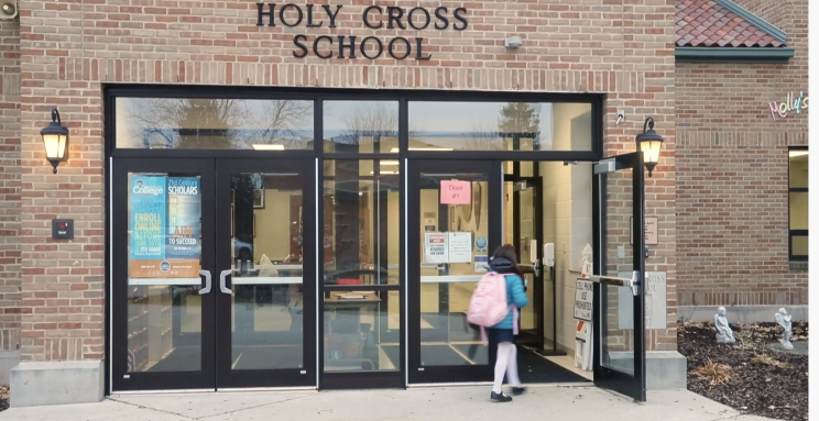 Exterior of Holy Cross School. A child is entering the building.