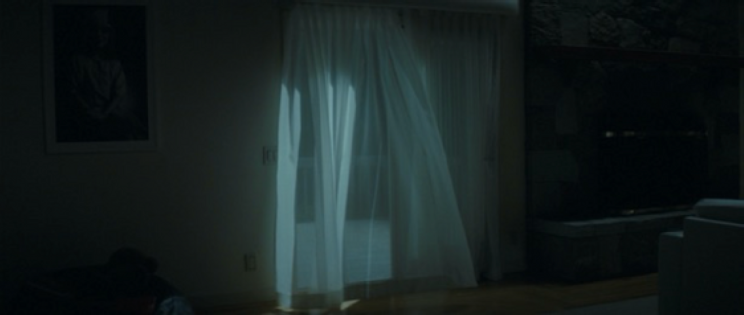 A dark room with a sliding glass door to a balcony. Sheer curtains cover the door.